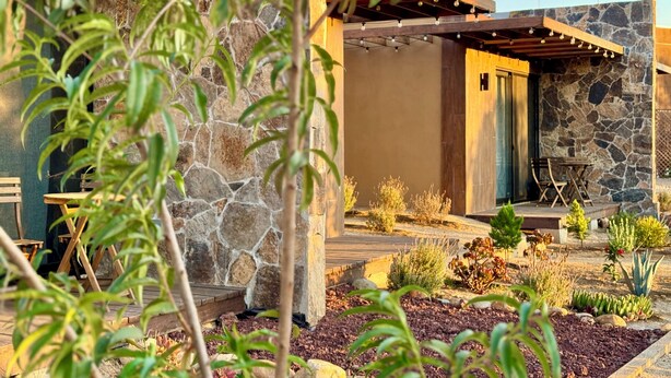A modern house with a stone facade, a wooden deck, and a garden with various plants. - Estancia Cataviña Valle de Guadalupe (Valle de Guadalupe)