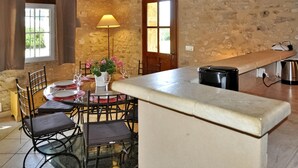 A rustic kitchen with a stone wall, a wooden bench, a table with chairs, a floor lamp, and a kettle. - Le Mazet De Bious Sadous (Isle Sur La Sorgue)