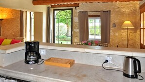A kitchen with a coffee maker, kettle, and a wooden cutting board. - Le Mazet De Bious Sadous (Isle Sur La Sorgue)