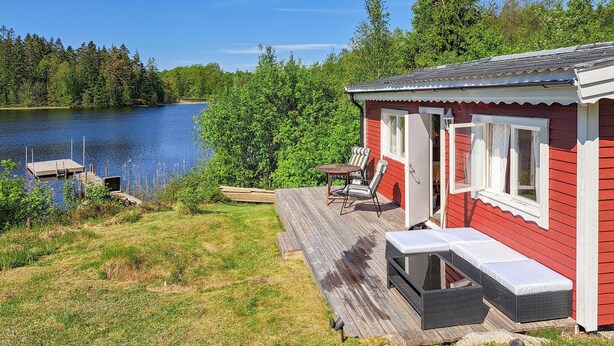 A red cabin with a deck overlooking a lake, a small dock, and a chair and table on the deck. - 3 bedroom gorgeous home in öxabäck (Öxabäck)