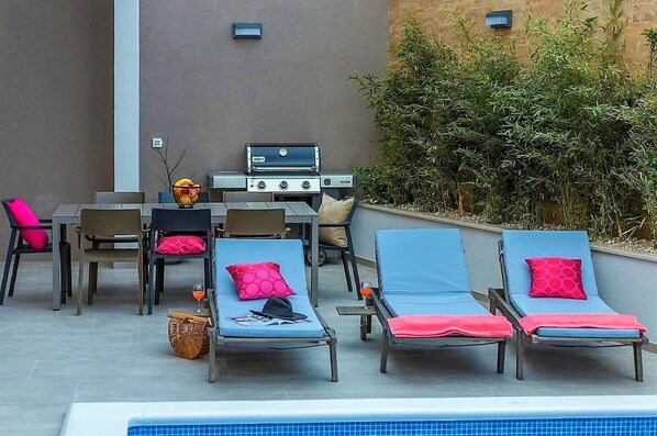 An outdoor pool area with lounge chairs, a barbecue grill, and a table with chairs. - Villa Aria with pool, 100m to beach (Tučepi)