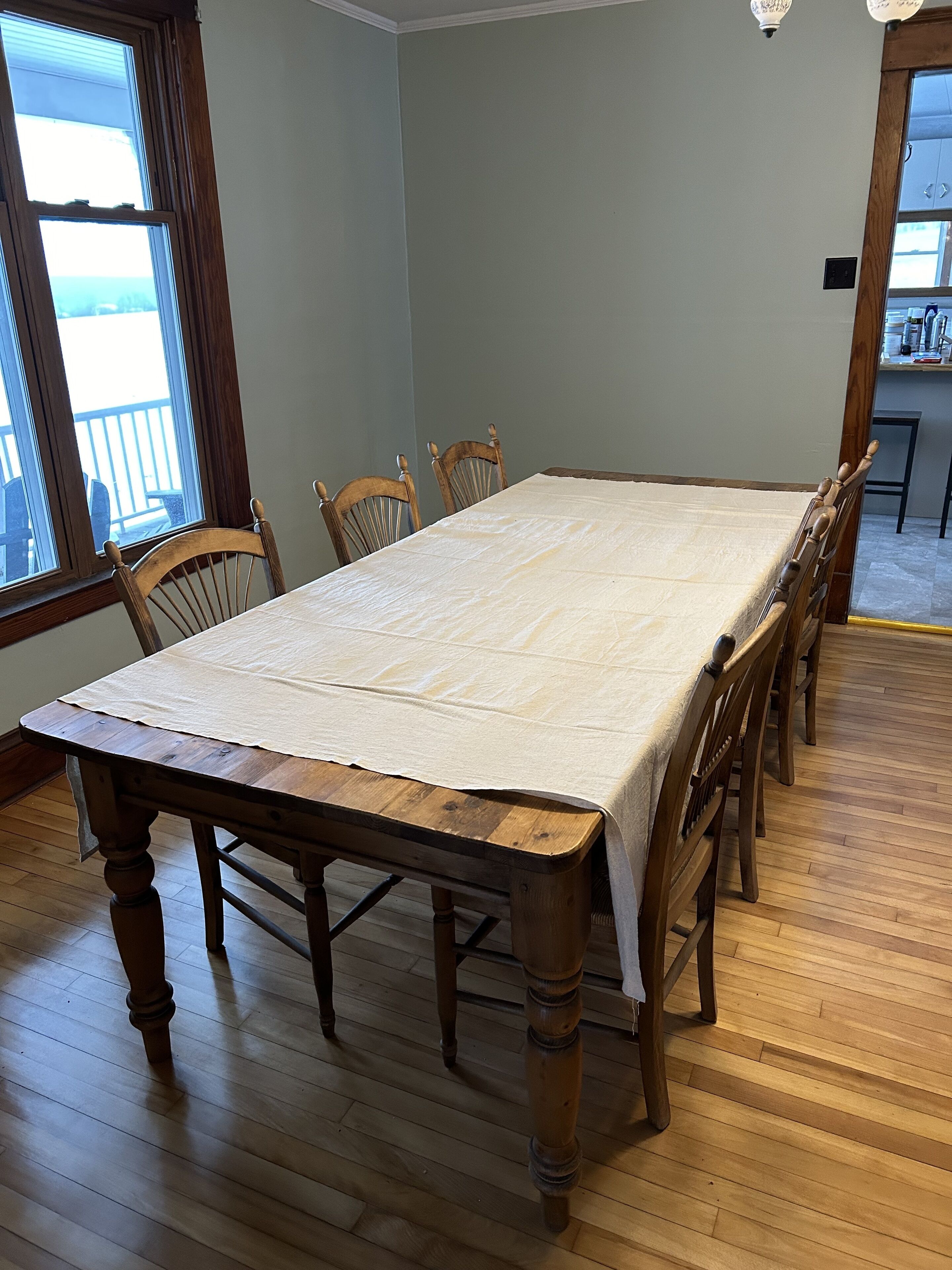 A dining table with a white tablecloth, wooden chairs, and a wooden floor.