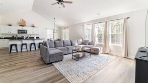 A spacious living area with a grey sectional sofa, a coffee table, and a kitchen area with white cabinets and a microwave. - Modern NC Home: Dock, Karaoke, Games, Fire Pit (Oriental)