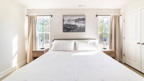 A bedroom with a large bed, two bedside tables, a nightstand, a window with curtains, and a framed picture on the wall. - Modern NC Home: Dock, Karaoke, Games, Fire Pit (Oriental)