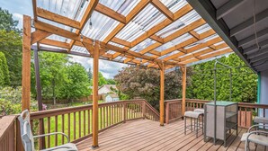 Una terraza de madera con pérgola, mobiliario exterior y vistas a un jardín.
