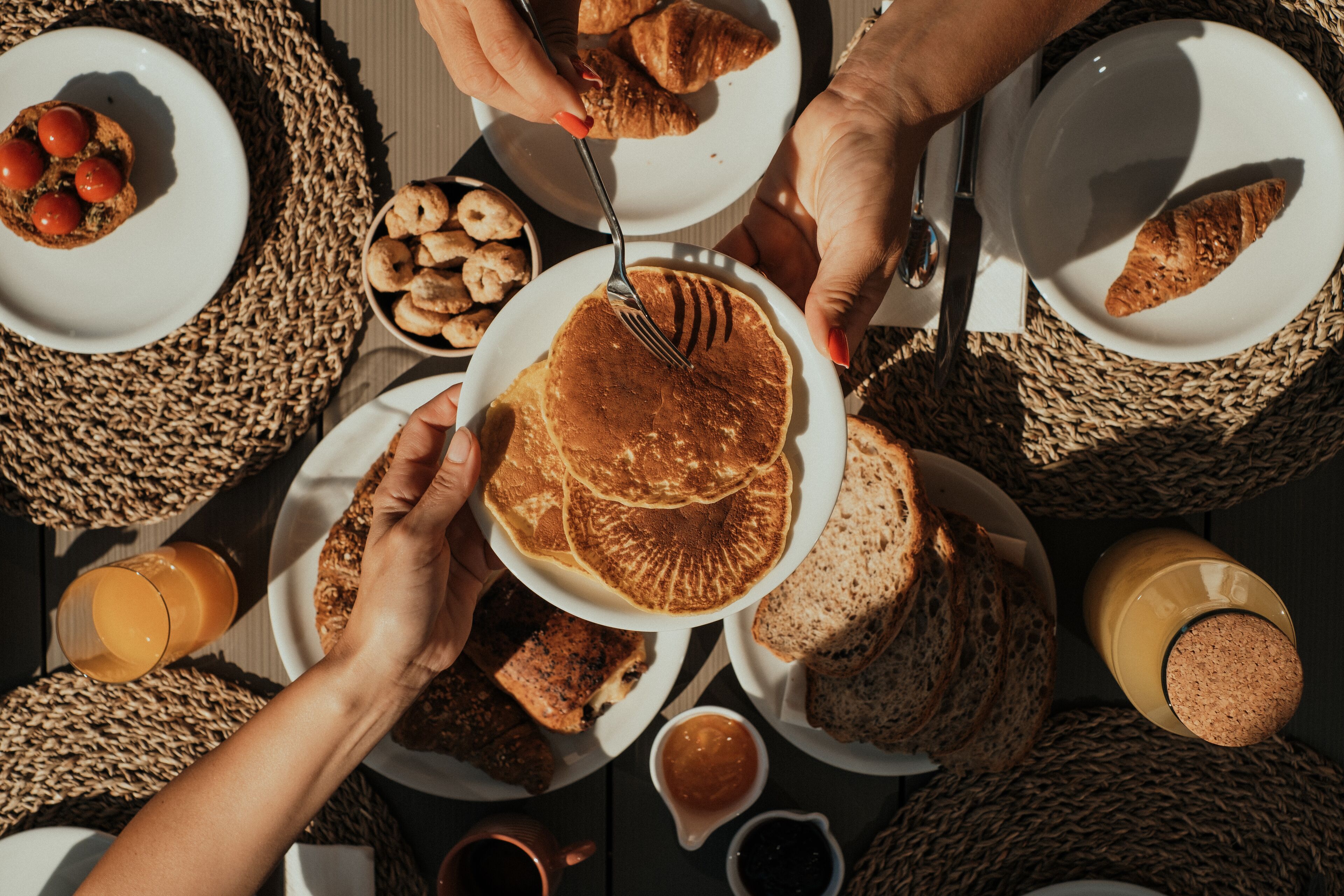 Ein Frühstückstisch mit verschiedenen Speisen auf Tellern, darunter Pfannkuchen, Croissants und Brot.