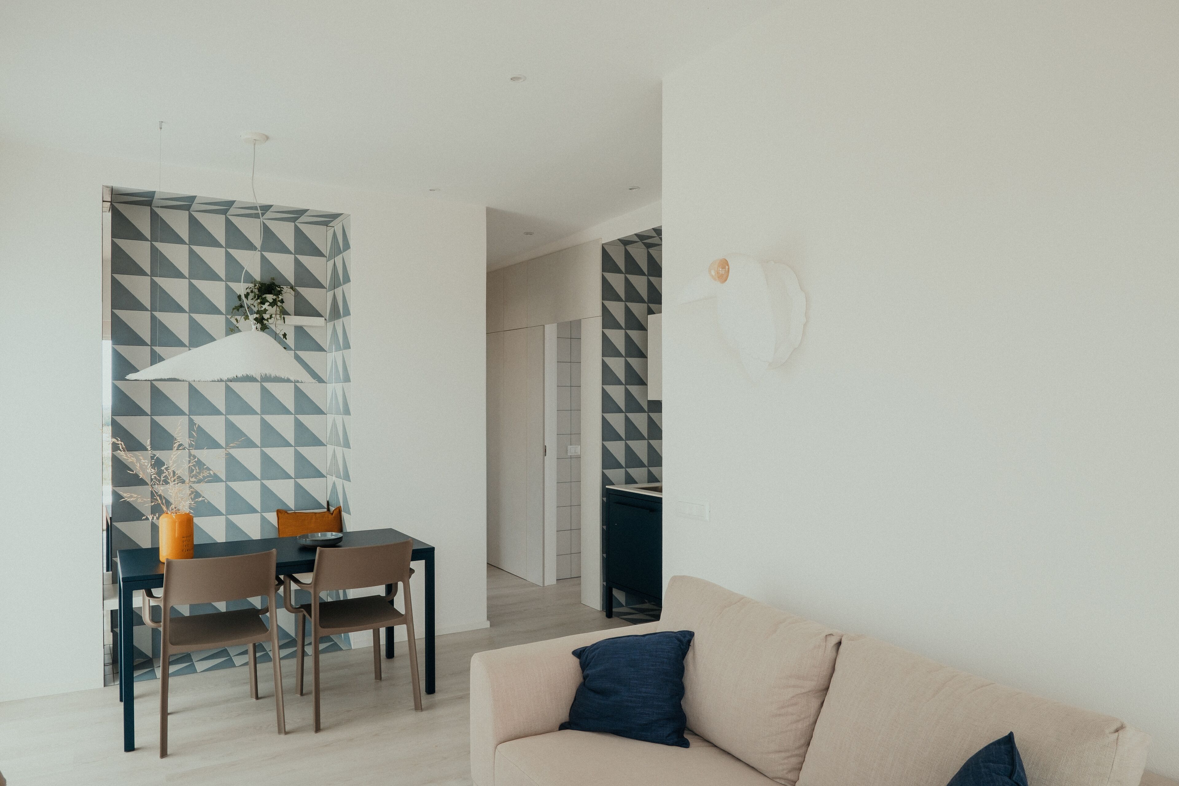 Un salon moderne avec un canapé beige, un coin repas comprenant une table et des chaises, et une cuisine visible à travers une porte ouverte.