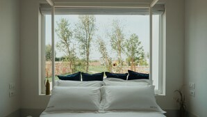 A bedroom with a large window, white bedding, and a view of trees and a brick wall. - METHE Resort (Lizzano)