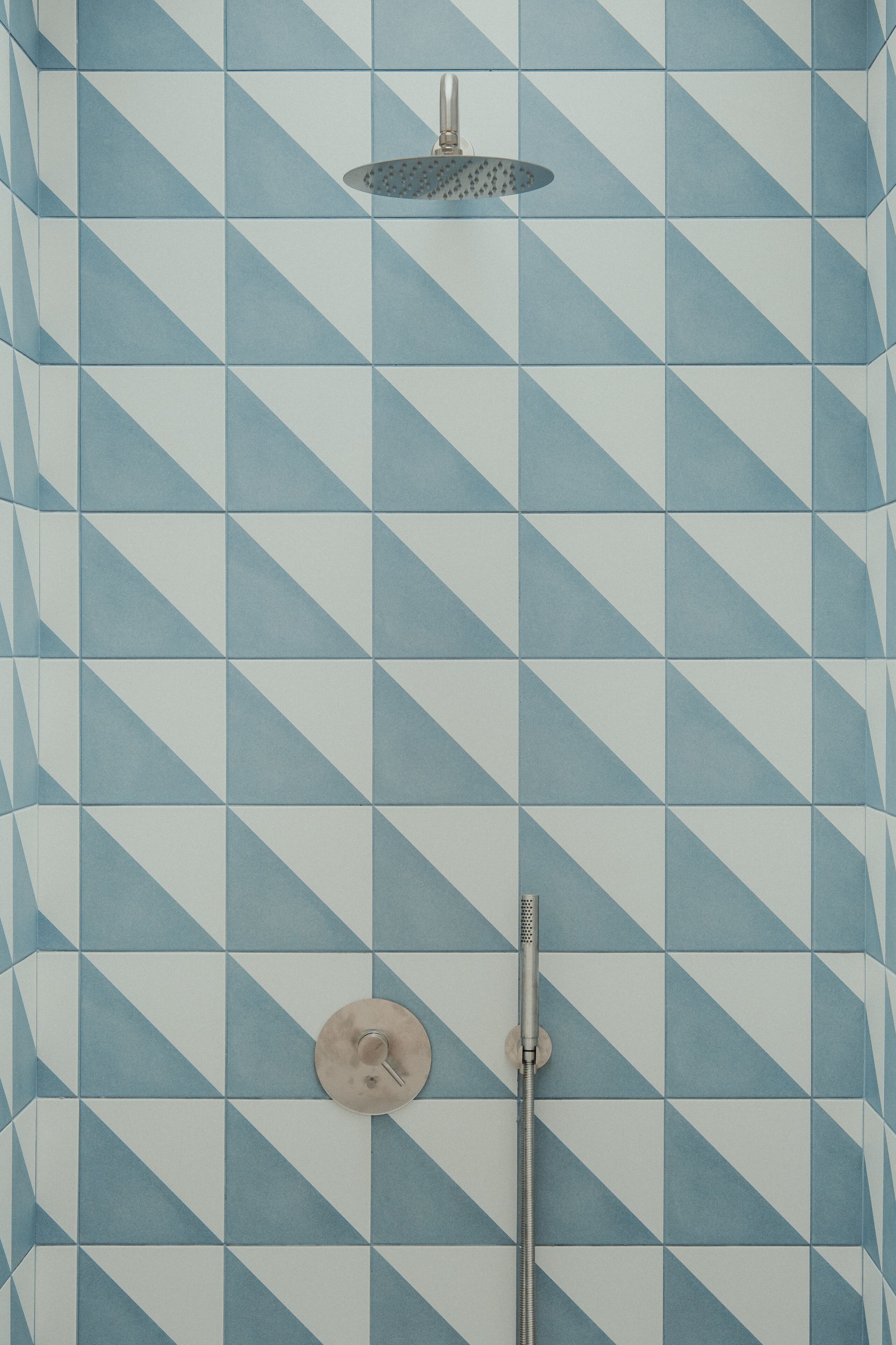 Une salle de bain avec un carrelage aux motifs géométriques et une douche dotée d’un panneau de commande circulaire et d’un pommeau de douche à main.