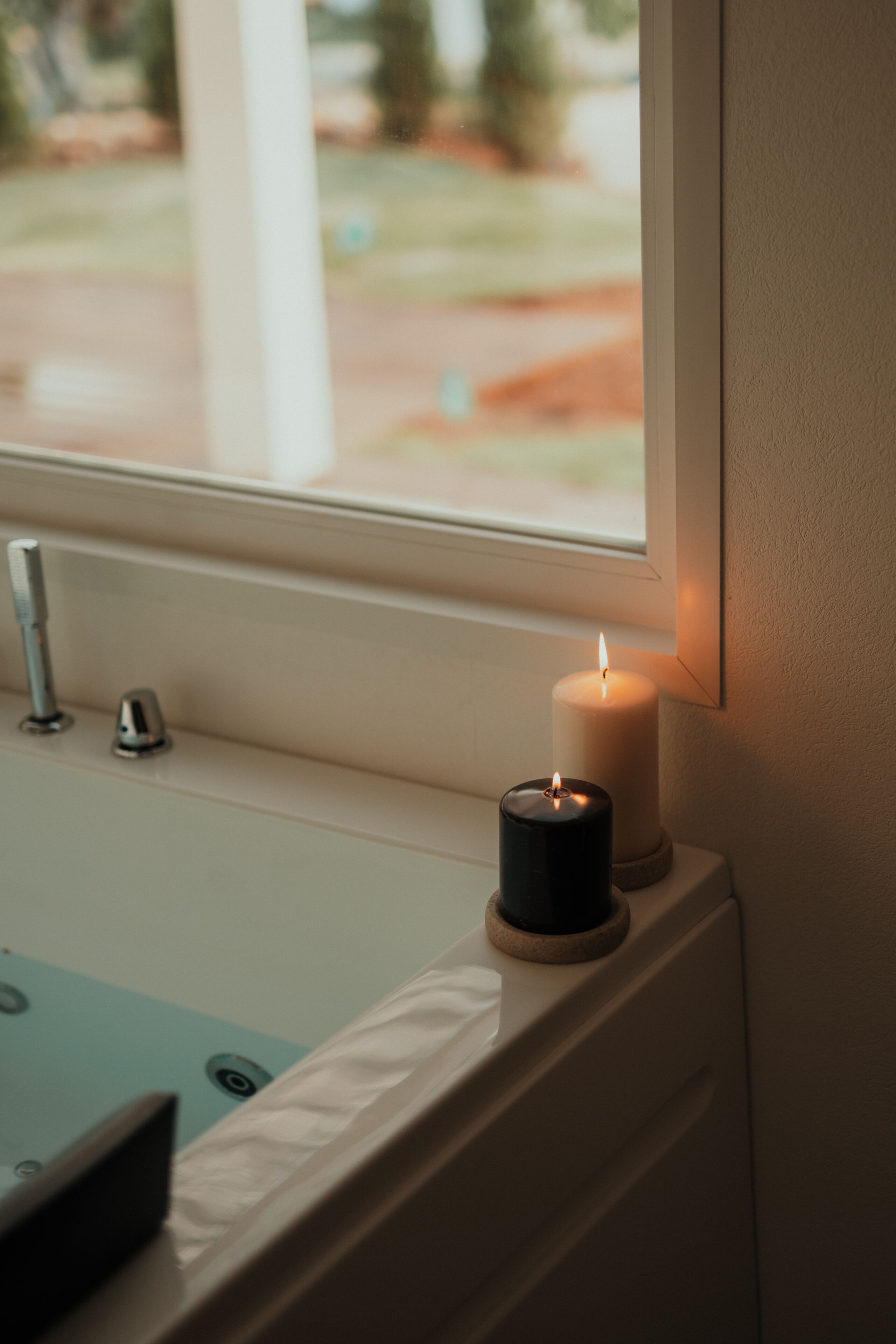 Une salle de bain avec une baignoire, une fenêtre et deux bougies posées sur le rebord de la fenêtre.