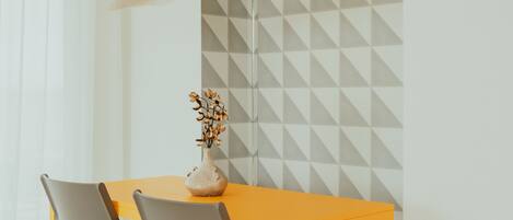 A dining area with a table and chairs, a vase with dried flowers, and a geometric-patterned wall.