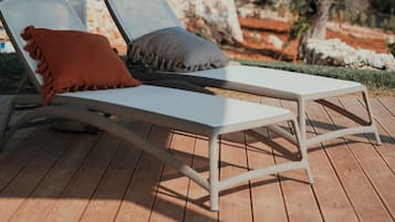 Relax in a serene outdoor setting with a hot tub and lounge chairs amidst olive trees.