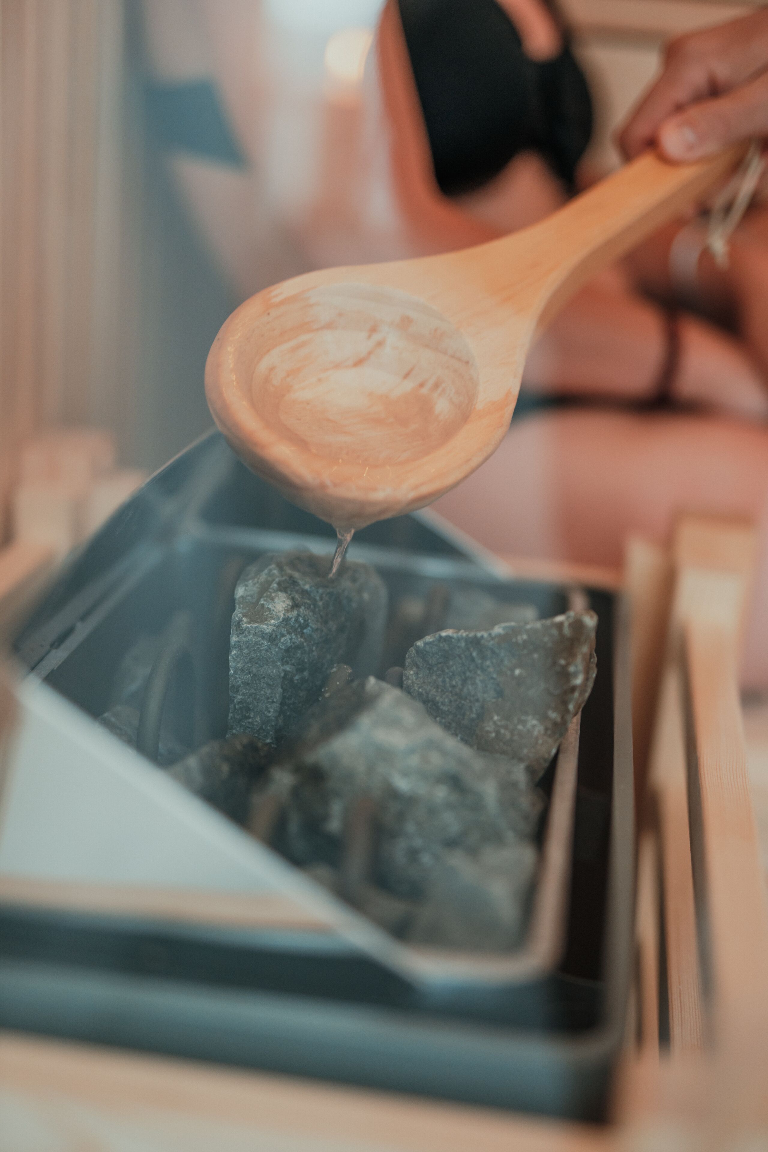 A wooden spoon lifting a charred piece of food over a grill.
