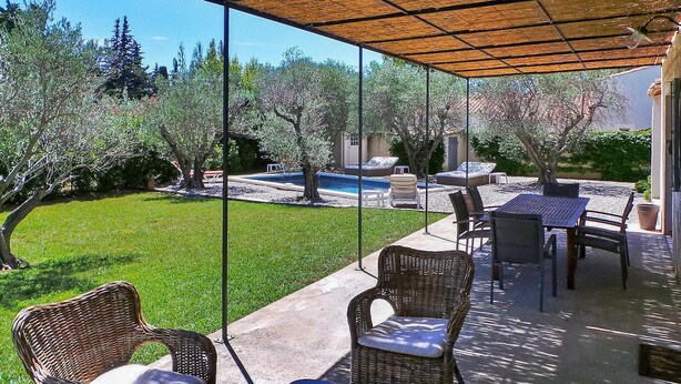 Um alpendre coberto com móveis de exterior, piscina e relvado.