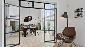 A modern kitchen with a dining area, large windows, and a cozy seating area with a lamp.