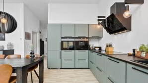 A modern kitchen with light green cabinets, a black countertop, and pendant lighting.