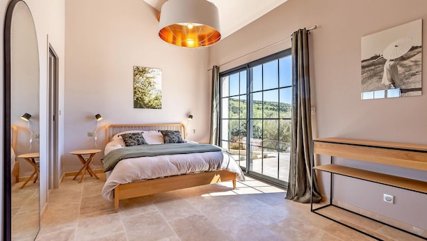 A spacious bedroom with a large bed, a desk, and a view of the outdoors through a large window. - Lovely home in Roussas (Roussas)