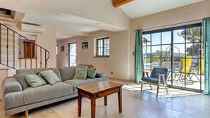 A spacious living area with a grey sofa, wooden coffee table, and a view of a patio with outdoor furniture. - Lovely home in Roussas (Roussas)