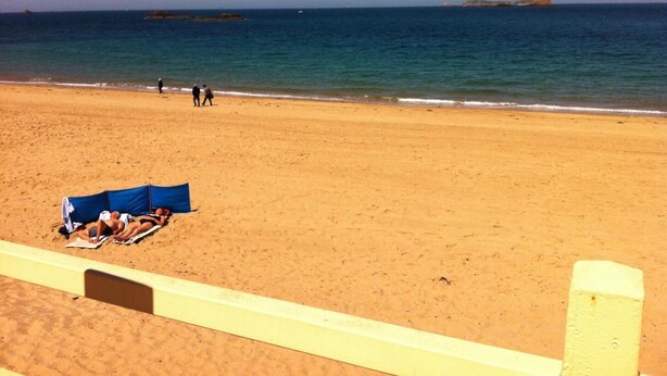 A beach with a sandy shore, a few people walking, and a blue tent set up.