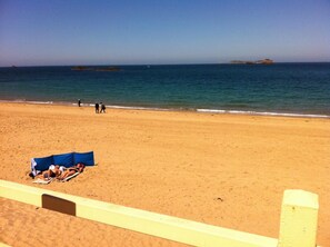 A beach with a sandy shore, a few people walking, and a blue tent set up.