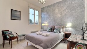 A bedroom with a large bed, a chair, a table, and a window.