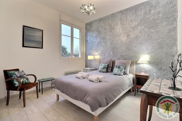 A bedroom with a large bed, a chair, a table, and a window.