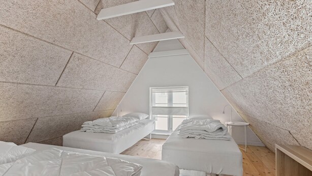 Een zolderkamer in een driehoekige vorm met twee bedden, een klein tafeltje en een raam.
