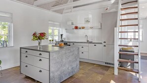 Een moderne keuken met witte kasten, een centraal eiland met lades, een inbouwoven en een houten trap.