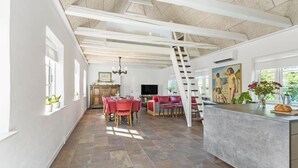 Een ruime woonkamer met een eettafel, rode stoelen, een televisie en een schilderij aan de muur.
