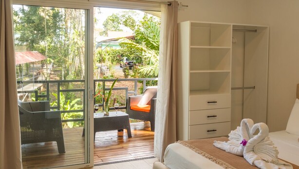 A bedroom with a bed, a wardrobe, a ceiling fan, and a sliding glass door leading to an outdoor area with a table and chairs. - Secluded Tropical Home in La Fortuna (La Fortuna)