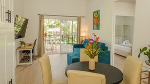 A modern hotel room with a dining area, a TV, a sofa, a bed, and a balcony with a view of greenery. - Secluded Tropical Home in La Fortuna (La Fortuna)