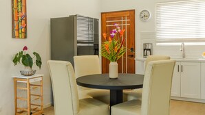 A dining area with a round table, four chairs, a vase with flowers, a refrigerator, a clock, and a window with blinds. - Secluded Tropical Home in La Fortuna (La Fortuna)