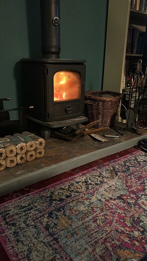 Un poêle à bois avec des bûches, un panier en osier et un tapis à motifs dans une pièce.