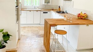Une cuisine moderne avec des meubles blancs, un îlot central en bois et une fenêtre qui laisse entrer la lumière naturelle.