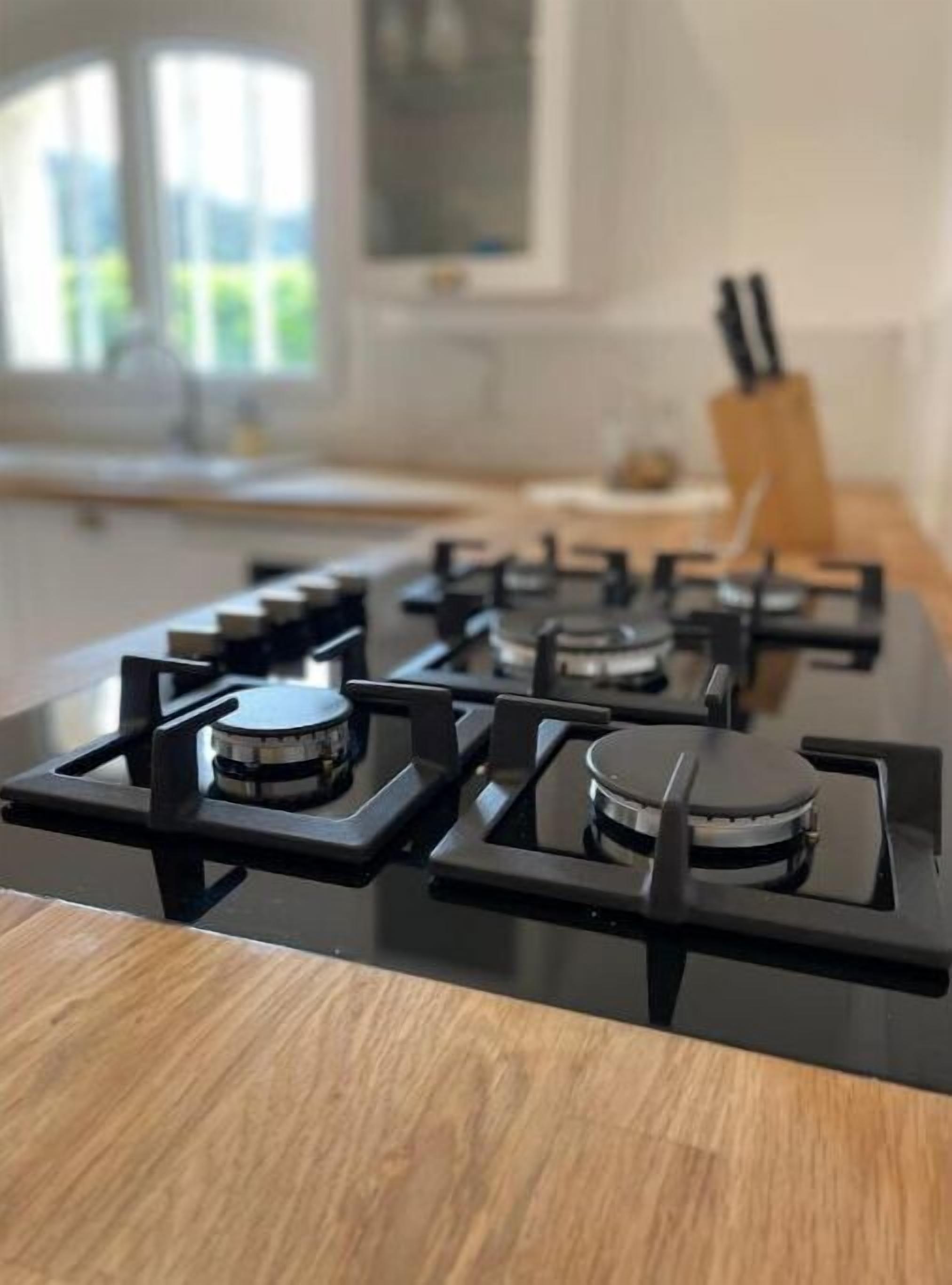 A kitchen with a gas stove, wooden countertop, and a window with a view of greenery.