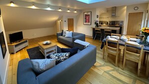 A modern living room with a grey sofa, a coffee table, and a TV. There is a skylight above the sofa and a kitchen area with a dining table and chairs. - fantastic 2 bedroom with secure parking in Edinburgh's New Town (Edinburgh)