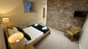 Een slaapkamer met een bed, een stoel, een stenen muur, een raam en een televisie.