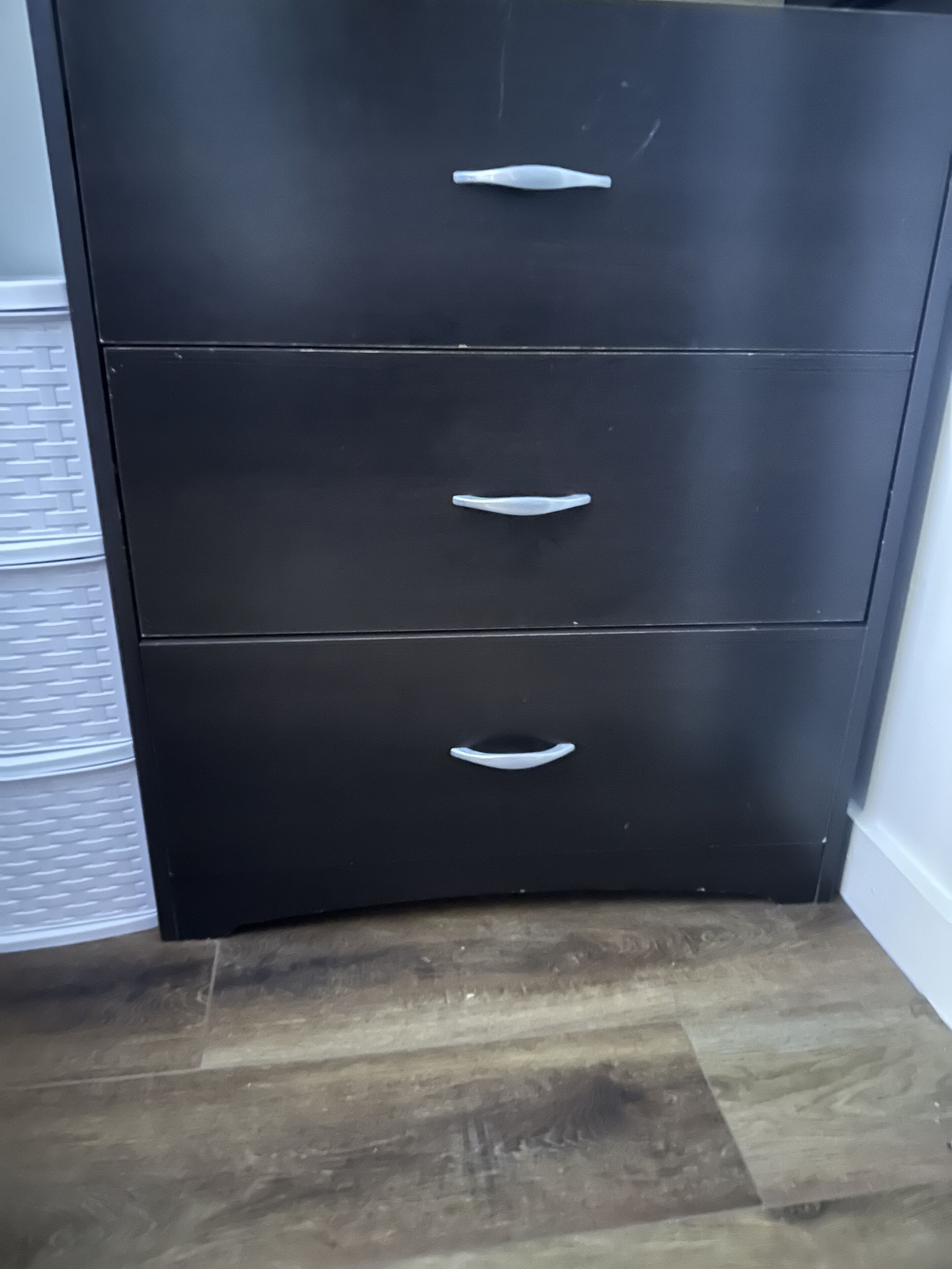 Une armoire noire avec trois tiroirs et deux poignées.