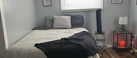 Une chambre à coucher avec un lit, une fenêtre avec des stores, une table de chevet avec une lampe et un mur orné de citations encadrées.