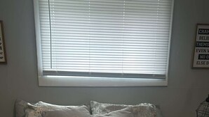 Un dormitorio con cama, almohadas y ventana con persianas.