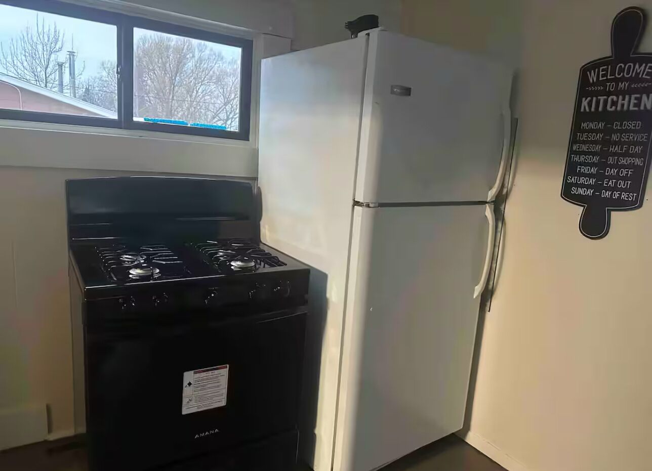 A kitchen with a stove, refrigerator, and a welcome sign listing the kitchen's weekly schedule.