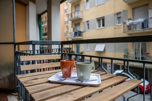 Ein Holztisch mit zwei Tassen auf einem Tablett, eine Bank und ein Balkongeländer.