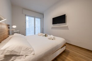 A modern hotel room with a bed, a TV, a desk, and a window.
