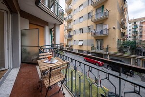 Ein Balkon mit Tisch und Stühlen, Blick auf eine Straße mit Autos und ein Gebäude mit Balkonen und Fenstern.