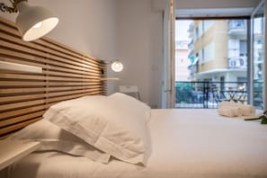 Ein Hotelzimmer mit hölzernem Kopfteil, einem Bett mit weißen Leinen, einem Nachttisch und Blick auf den Balkon.