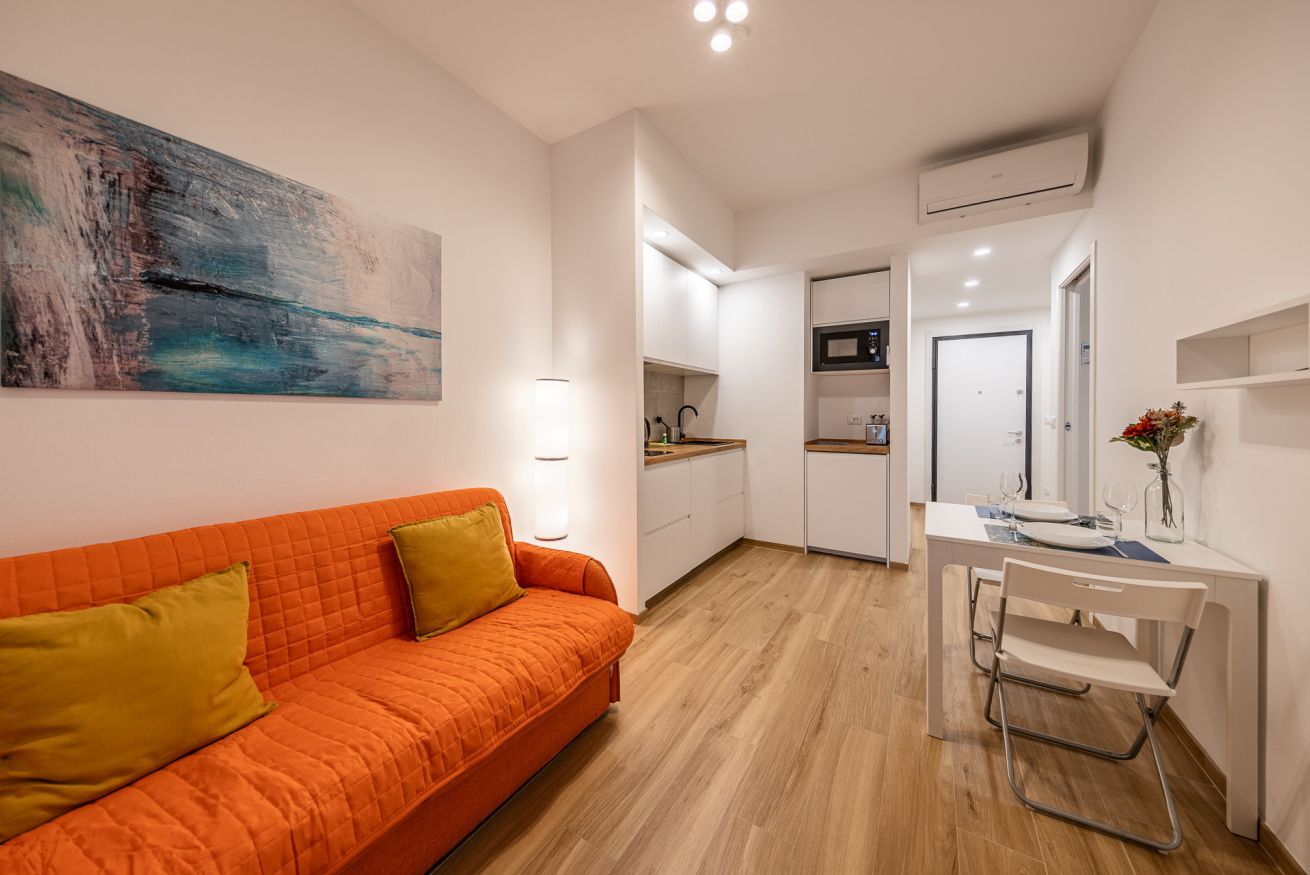 A compact living space with a kitchenette, a dining area, and a sofa with cushions.