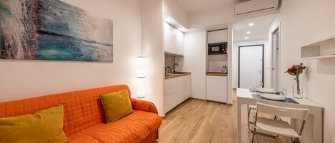 A compact living space with a kitchenette, a dining area, and a sofa with cushions.