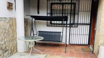 Un espace patio aménagé avec une table en verre, un banc et une chaise suspendue en métal.