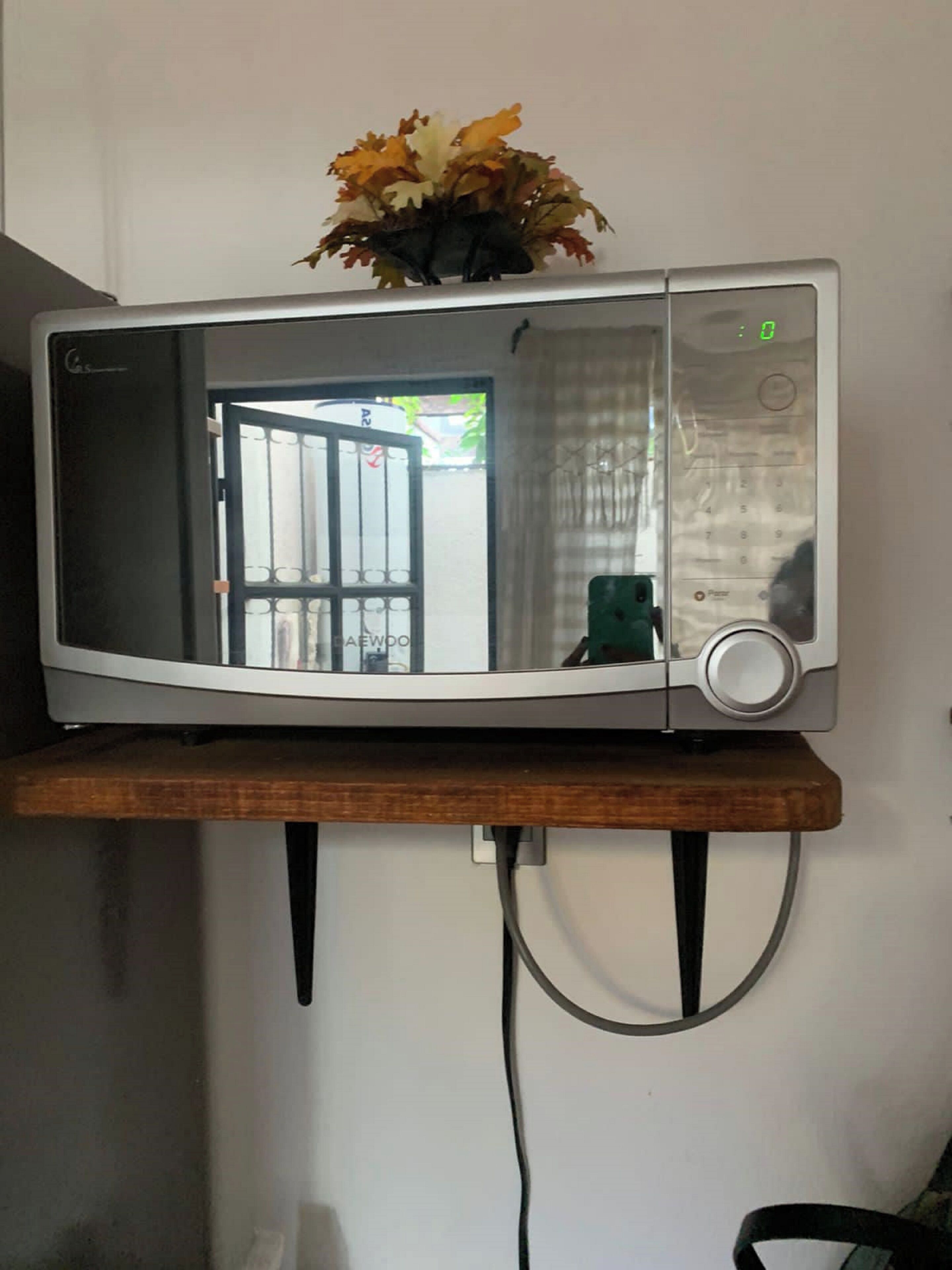 A microwave on a wooden shelf with a visible door and control panel.
