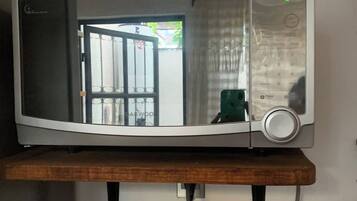 A microwave on a wooden shelf with a visible door and control panel.